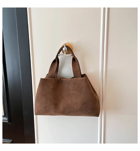 Detail of a dark brown suede tote bag featuring a wide handle and minimalist aesthetic