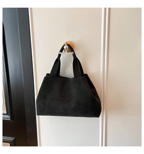 Detail of minimalist black suede tote bag with wide shoulder strap hanging on white wall