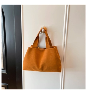 Detail of soft orange suede tote bag with wide shoulder strap hanging on a wall