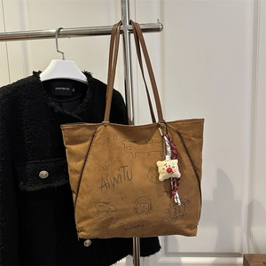 Brown suede tote bag with cartoon print and plush charm hanging on a rack