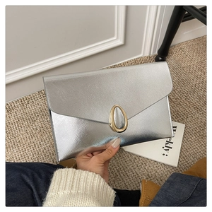 Detail of silver envelope clutch featuring brushed metallic texture and gold oval buckle