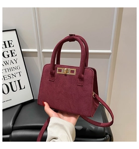 Detail of burgundy matte suede handbag with golden rectangular lock and twin handles