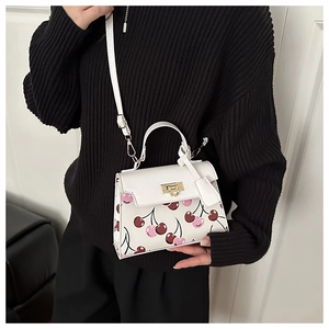 Close-up of white cherry print handbag featuring gold metal turn-lock and leather texture