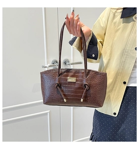 Detail of dark brown croc-pattern leather tote with gold logo and twisted handle detail