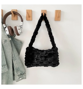 Detail of black faux fur bag with woven texture hanging on a minimalist wall hook