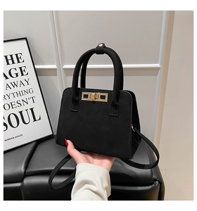 Close-up of black suede tote bag featuring golden twist lock and cylindrical handles