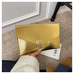 Detail of golden envelope clutch bag featuring crosshatch texture and oval metal buckle