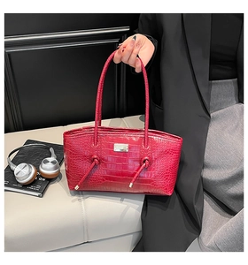 Detailed view of red crocodile embossed leather bag with knotted handle on a sofa