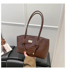 Detail of dark brown crocodile pattern handbag with gold logo plate and knotted handles