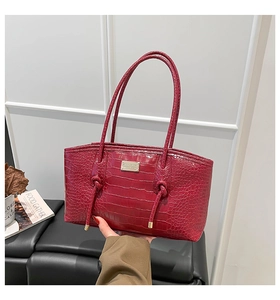Detail of dark red crocodile textured tote bag with metal plaque and drawstring knots