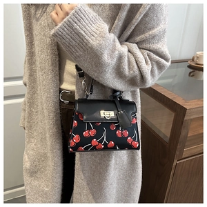Fashionable black shoulder bag with cherry print and golden lock worn by a model