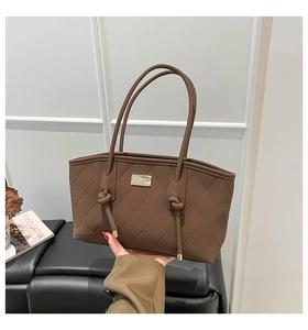 Detail of dark brown quilted tote bag with gold metal plaque and knotted handle design