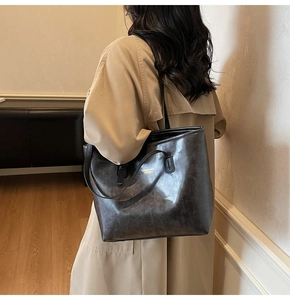 Detail of dark brown leather tote bag with gold lettering shown on shoulder with beige coat