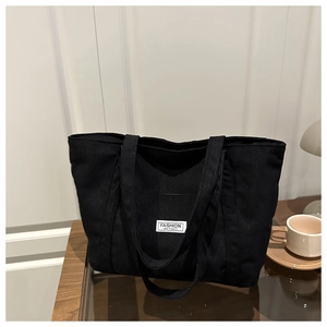 Detail of black corduroy tote bag with white Fashion Instinct label in a cozy setting