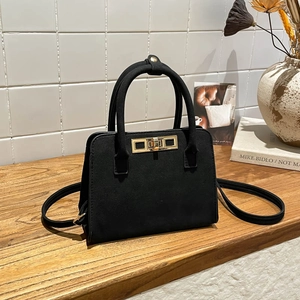 Retro black matte tote bag with gold rectangular buckle and top handle shown on a wooden desk