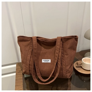 Close-up of brown corduroy tote bag showing ribbed texture and fashion label on desk