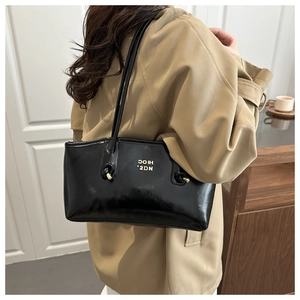 Detail of glossy black patent leather tote bag with gold logo and stylish knotted handles