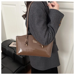 Detailed close-up of brown glossy leather shoulder bag with knotted strap and metal logo