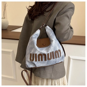 Detail of blue denim hobo bag with brown leather strap and stylish artistic letters