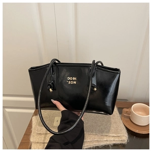 Detail of a black patent leather tote bag with gold metal accents on a stylish table