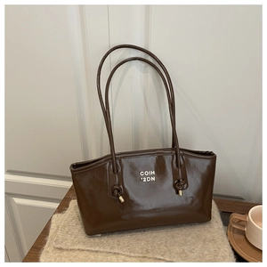 Detail of dark brown glossy tote bag with white lettering and gold metal hardware