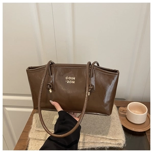 Detail of dark brown glossy leather tote bag with gold logo and stylish knotted strap