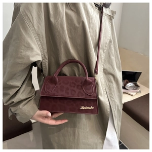 Dettaglio borsa bordeaux con stampa leopardata e logo dorato portata da modella in trench