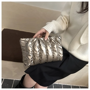 Detail of metallic quilted padded envelope clutch bag held by model for 2025 winter style