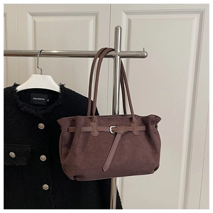 Detail of dark brown matte suede tote bag with silver buckle strap hanging on a hanger
