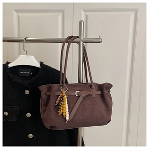 Macro detail of dark brown faux suede tote bag with leather buckle and beaded tassel