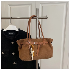 Detail of brown suede tote bag with leather buckle strap and wooden bead pendant