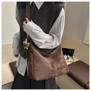 Brown leather hobo bag with teddy bear charm and silk scarf detail on wide shoulder strap