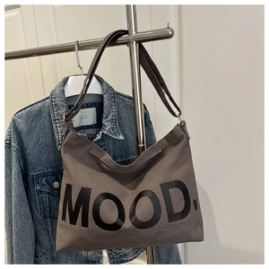 Dettaglio della borsa tote in tela marrone con scritta MOOD accanto a una giacca di jeans