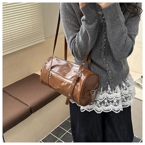 Detail of a brown cylinder Boston bag in glossy PU leather with silver metal buckles