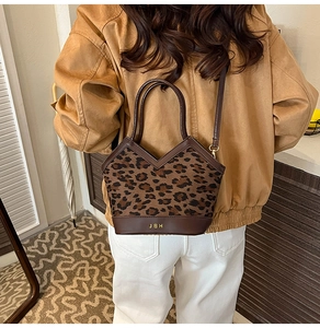 Detail of leopard print bucket bag with gold logo and leather strap worn by a model