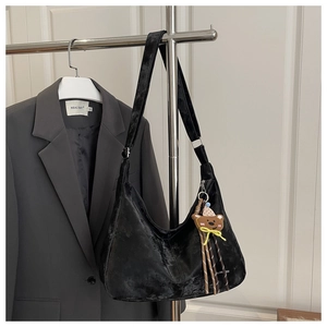 Detail of black velvet hobo bag with cute bear charm hanging on a metal rack