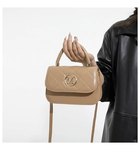 Detalle de bolso bandolera acolchado beige con logo M dorado y asa sobre chaqueta negra