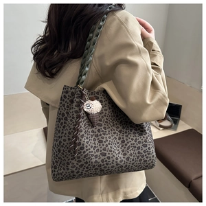 Detail of leopard print tote bag with green braided handle and decorative charm