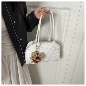 Detail of white quilted bowling bag with plush monster charm and smooth zipper