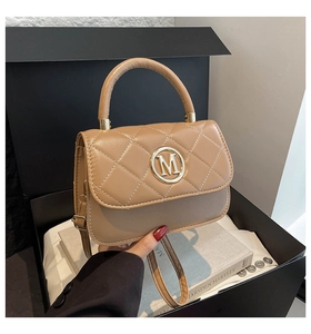 Detalle de bolso acolchado caqui con hebilla dorada logo M en una caja de regalo premium