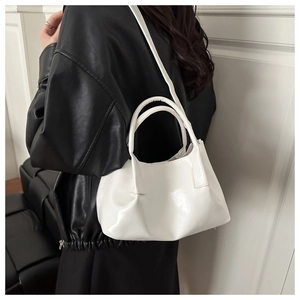 Close-up of white glossy bucket bag with pleat details worn over a black leather jacket