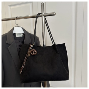Detail of a black suede tote bag featuring slim straps and a creative cookie pendant charm