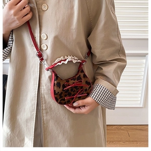 Detalle del mini bolso de leopardo con lazos de cuero rojo y asa ondulada sobre gabardina