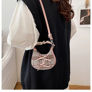 Detail of checkered crescent bag with pink leather trim and bow accents on a model