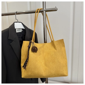 Detail of yellow suede tote bag with textured surface and decorative braided keychain