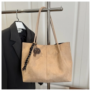Detail of suede tote bag with woven knot and vintage metal charms on a shoulder strap