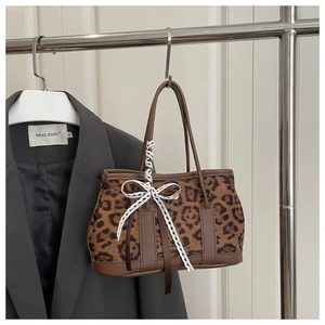 Detail view of leopard print tote bag with white lace bow and brown leather handles