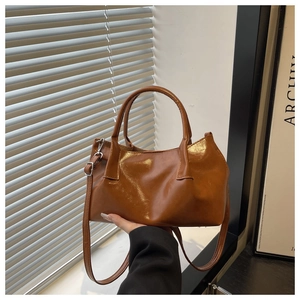 Detail of glossy brown leather tote bag with silver buckle and adjustable shoulder strap