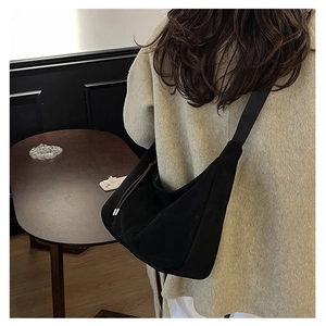 Black hobo tote bag with wide strap shown on model shoulder in warm interior