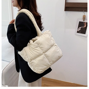 Detail of cream quilted tote bag with padded strap on a model wearing a black blazer